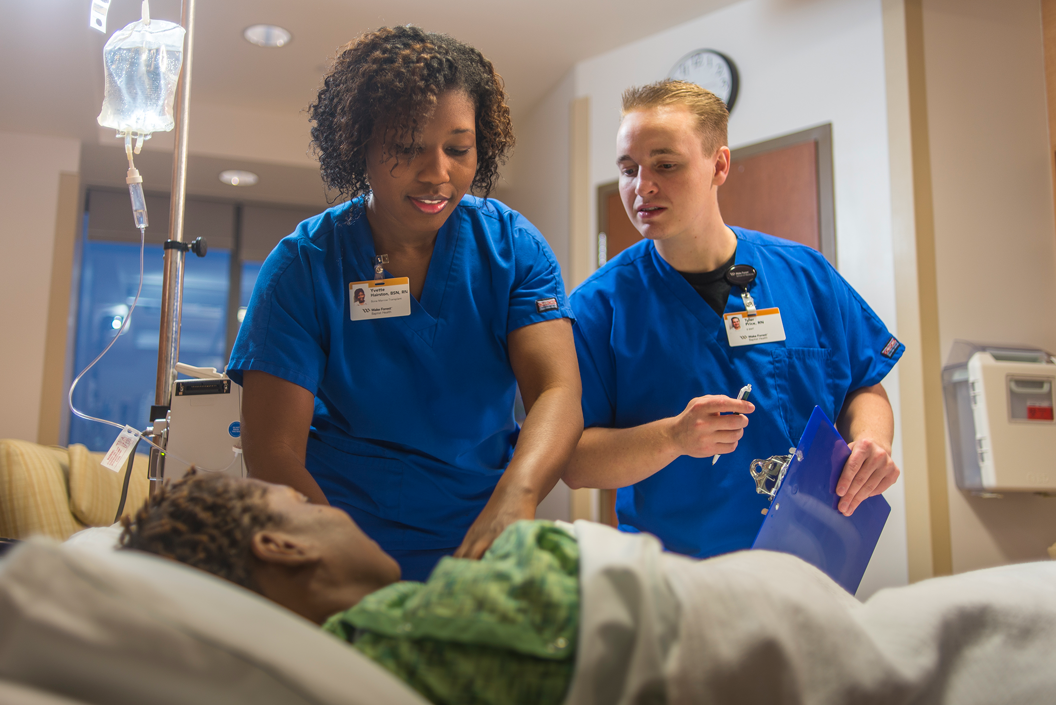 Nurse teaching another nurse alongside a patient bed in hospital room